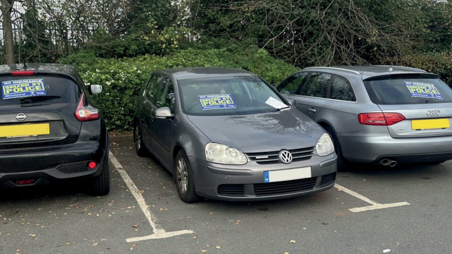 Three cars in a car park with stickers reading “No insurance, seized by police” on their windows.