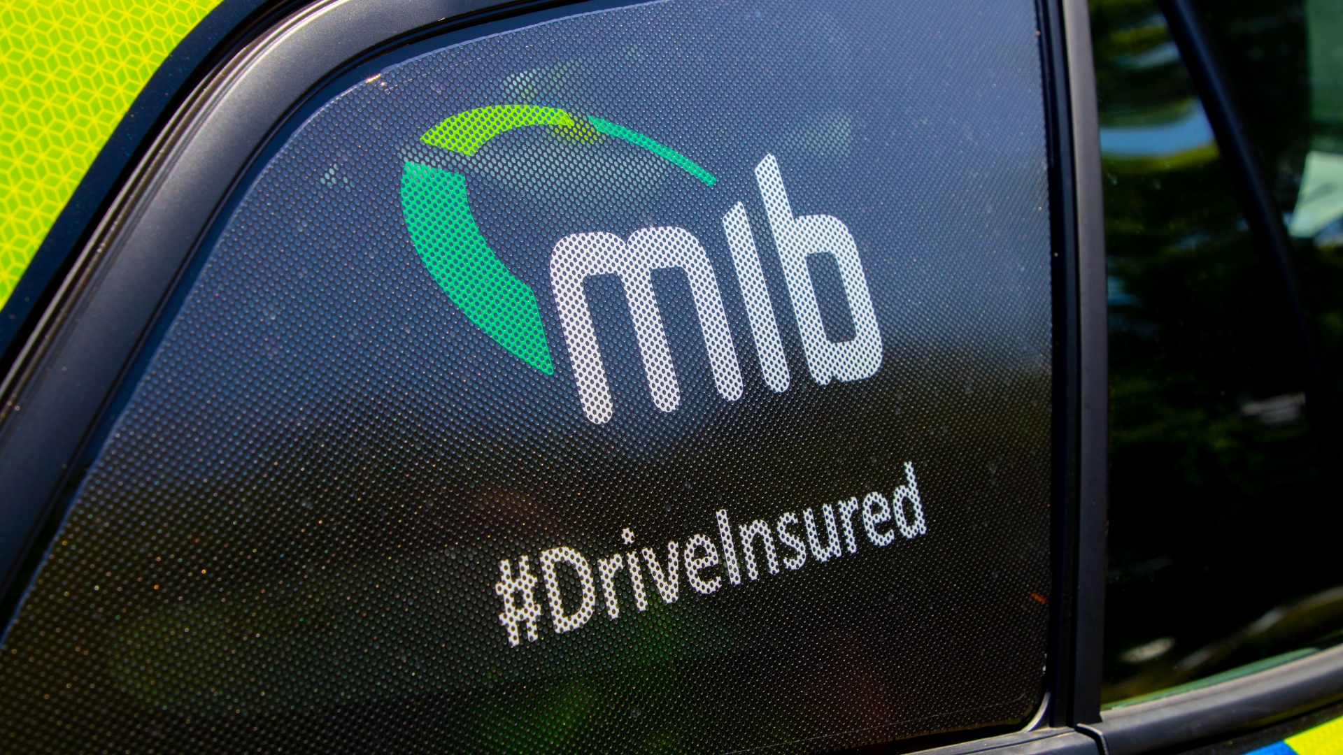 Car window with “MIB” logo and “#DriveInsured” text.