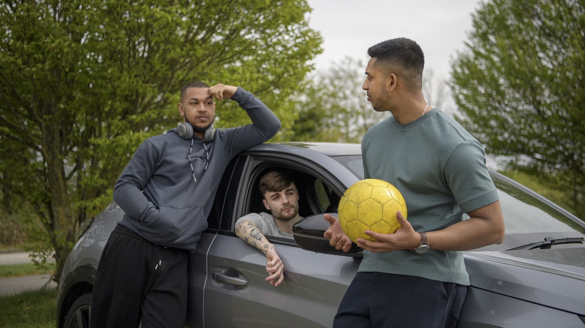 Three teenagers talking around a car