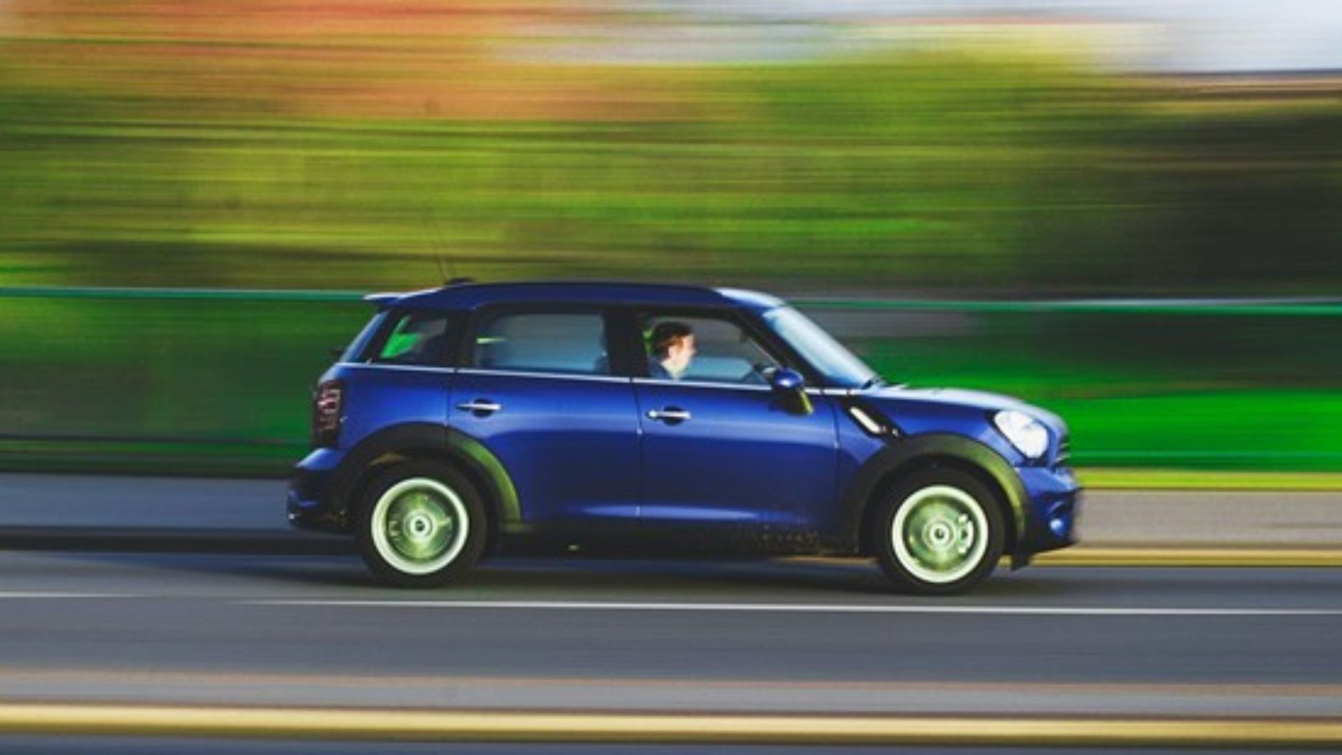 A blue mini drives along a road with a blurry background