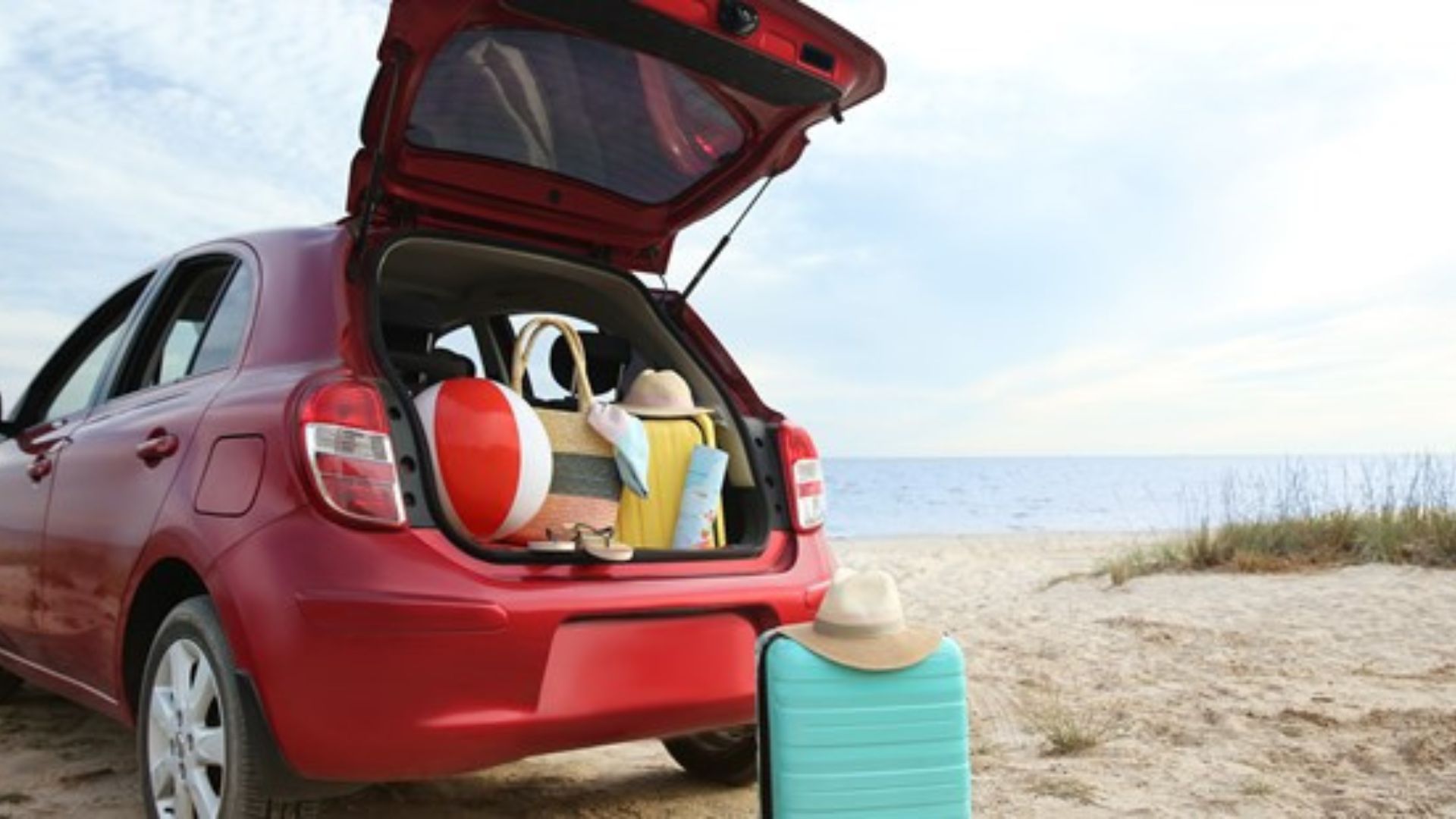 A red car on the beach with the boot open and luggage inside