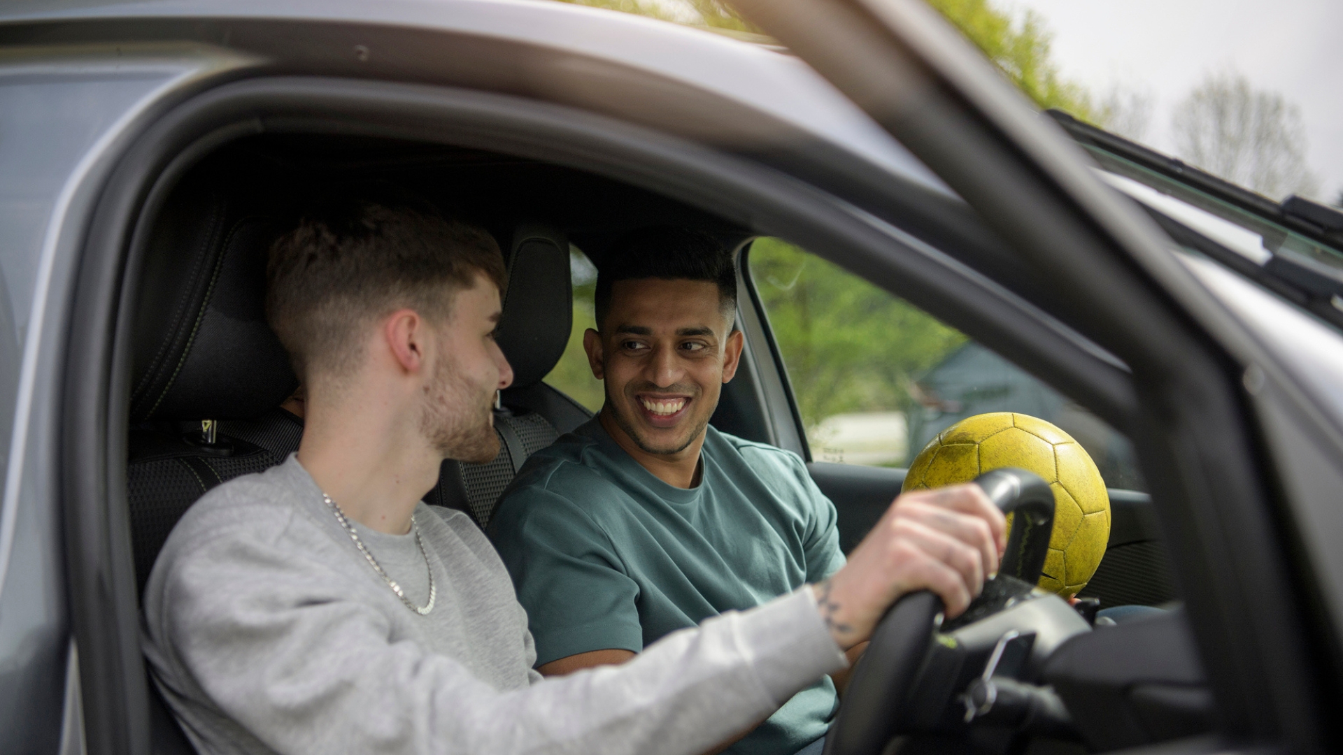 Two people sitting in a car talking, with  the person in the passenger seat holding a football.
