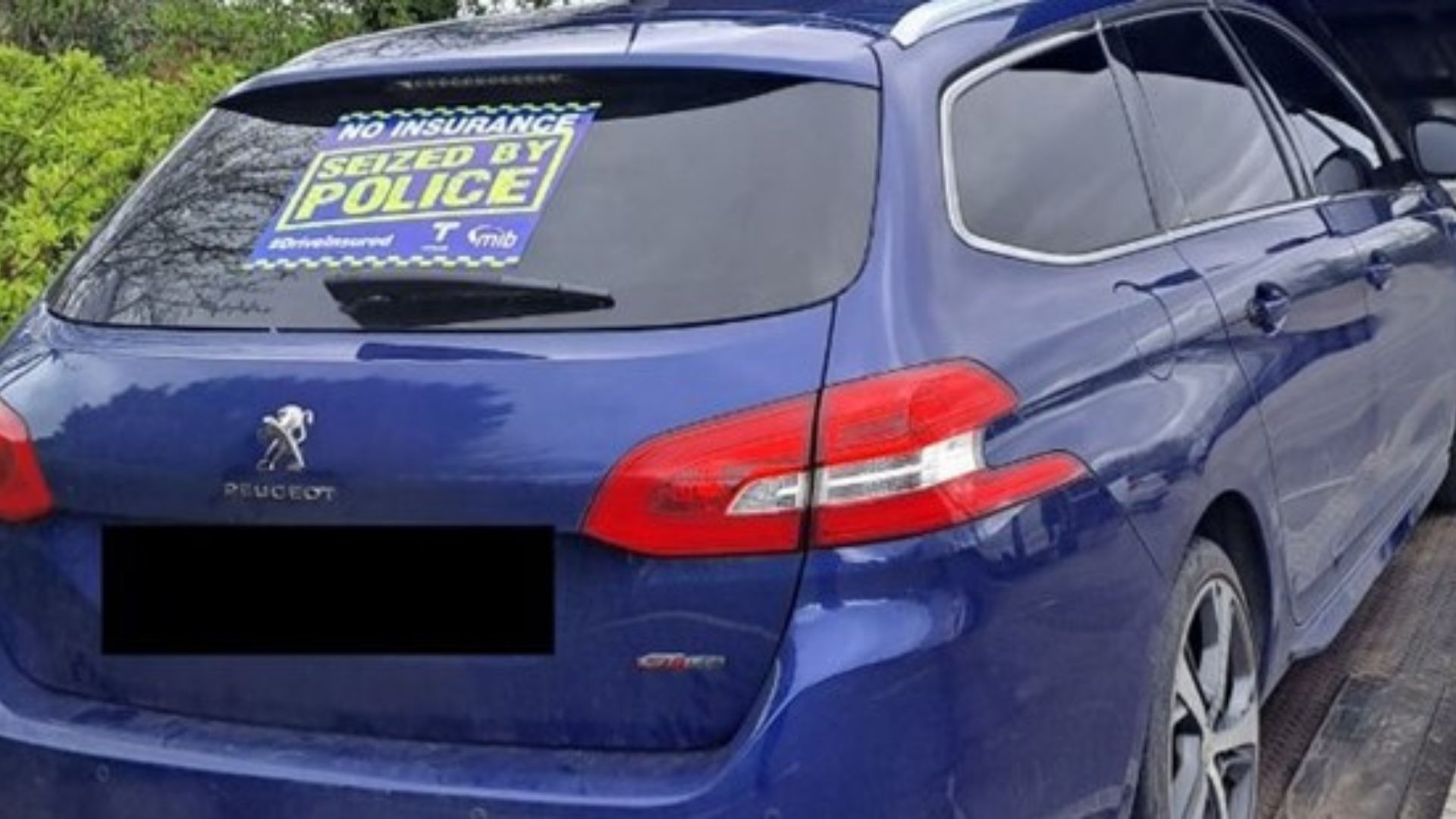 A blue Peugeot with a 'No insurance seized by Police' sticker on the back window.
