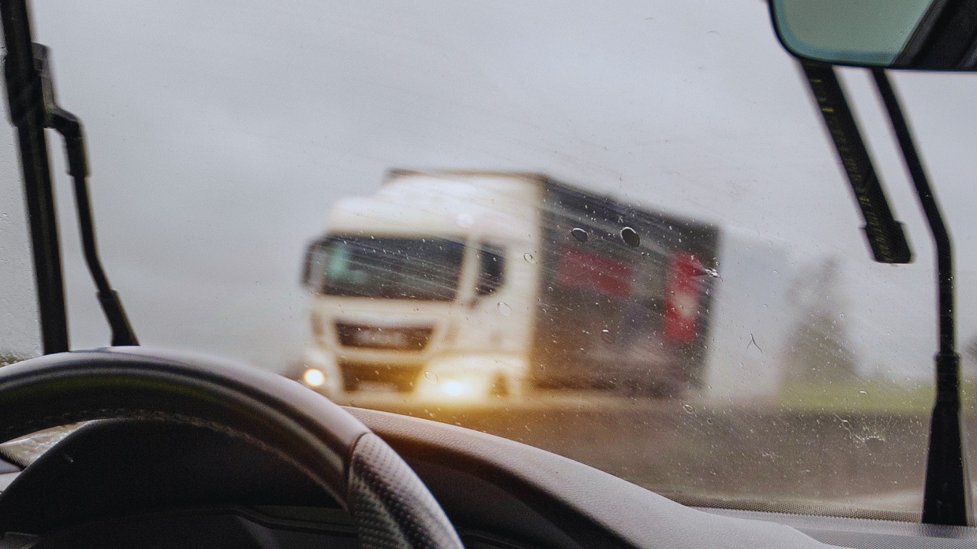 View from inside a car of a European lorry approaching on the left through a rain‑covered windscreen